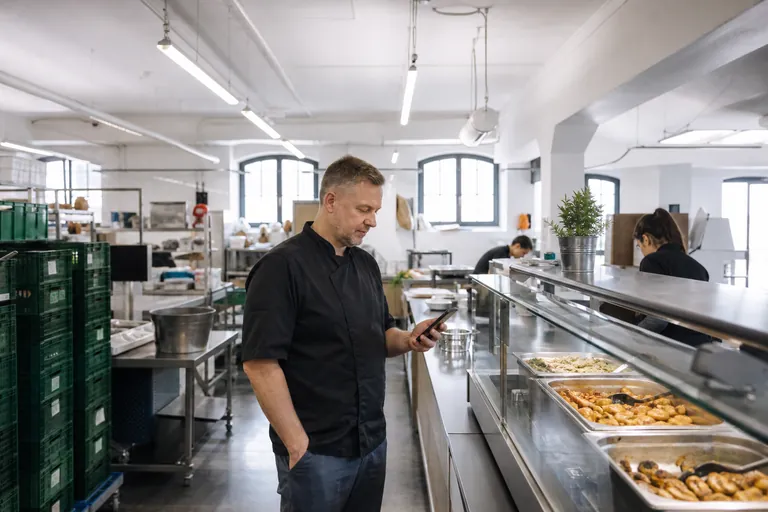 Ein Caterer prüft einen digitalen Wochenplan auf einem Smartphone an der Essensausgabe