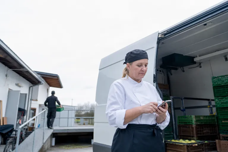 Eine Küchenmitarbeiterin aktualisiert unterwegs einen Wochenplan auf einem Smartphone