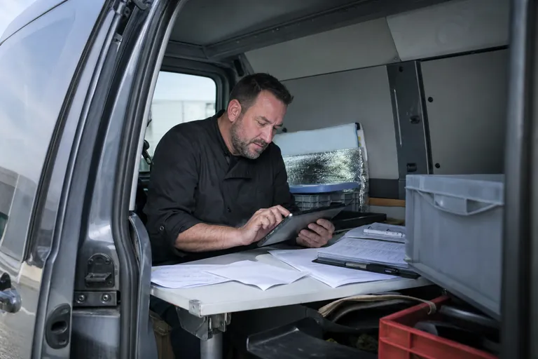 Ein Caterer prüft unterwegs Wochenplanunterlagen und Rechnungen auf einem Tablet