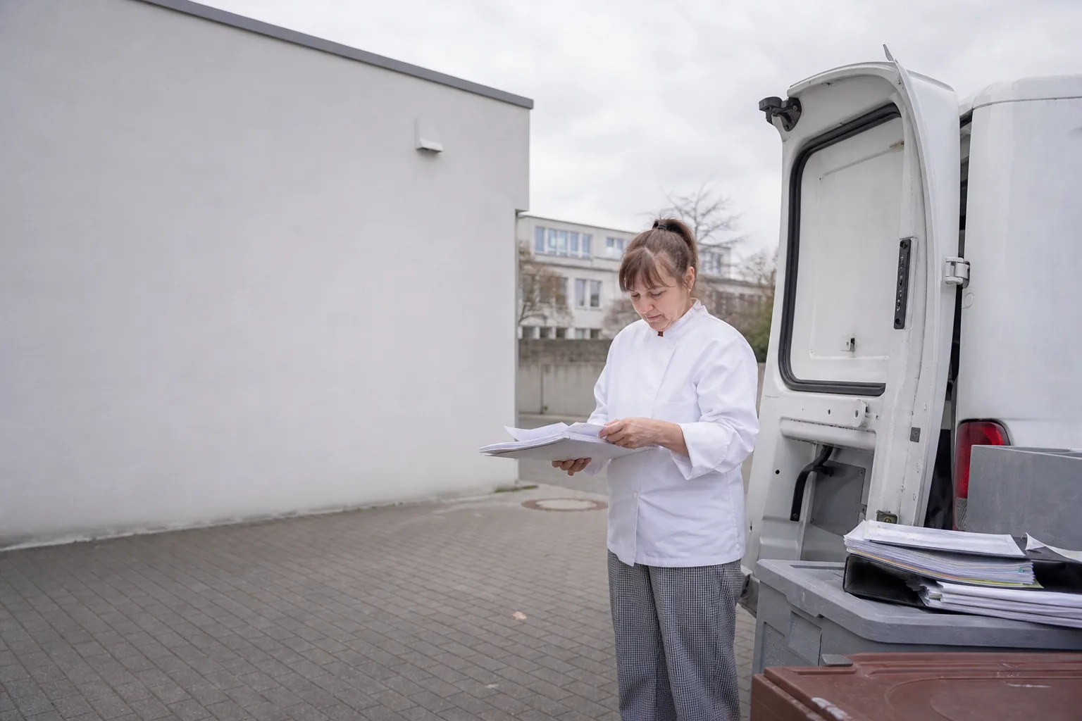 Mitarbeiterin einer Schulküche mit Wochenplan und Rezeptmappen auf einem Hof